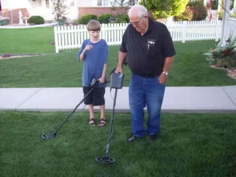 Grandpa and grandson are comparing their metal detectors and looking for old coins in the ground. 
